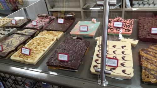 A display case filled with various colorful fudge and chocolate treats, labeled with names and prices.
