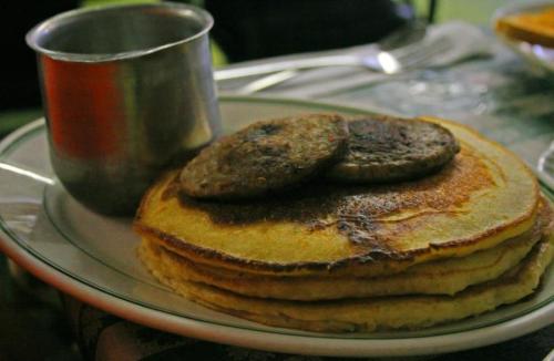 A plate of golden pancakes topped with two sausage patties, accompanied by a metal cup.
