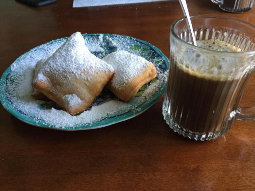 A plate of powdered sugar-dusted pastries next to a glass of coffee on a wooden table.