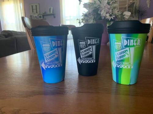 Three colorful travel mugs with "Granny's Diner" logo, displayed on a wooden table in a cozy room.