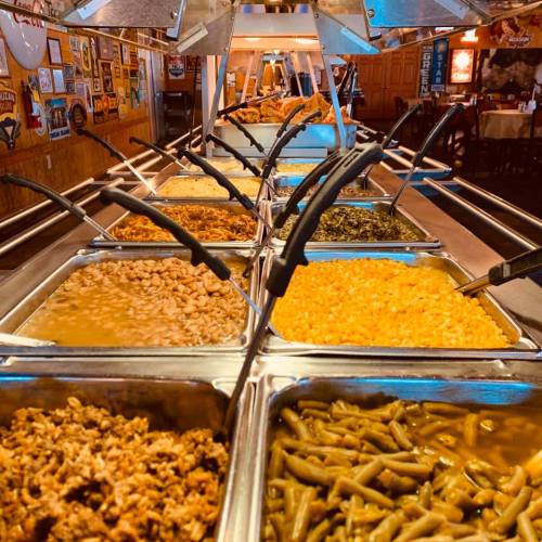 A buffet with various trays of food, including beans, greens, and meat, in a casual dining setting.