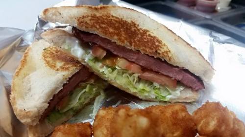 A toasted sandwich filled with lettuce, tomato, and sliced meat, served with crispy tater tots on the side.