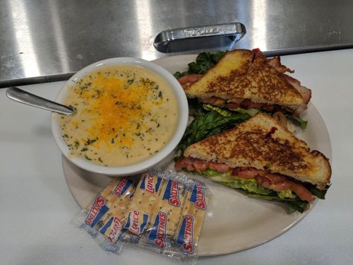 A plate with two grilled sandwiches, a bowl of creamy soup topped with cheese, and two packets of crackers.