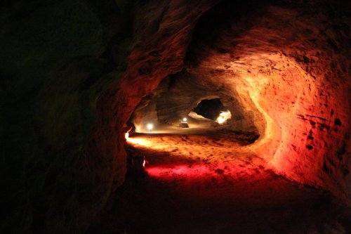 A dimly lit cave with colorful lights illuminating the rocky walls and sandy floor, creating a mysterious atmosphere.