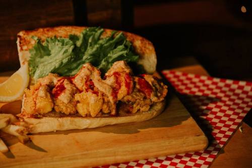 A delicious sandwich with crispy fried chicken, lettuce, and sauce, served with a lemon wedge on a wooden board.