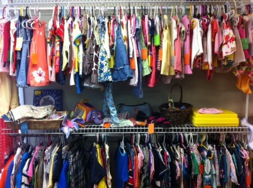 A colorful assortment of children's clothing hanging on racks, with baskets and bins of clothes on shelves below.