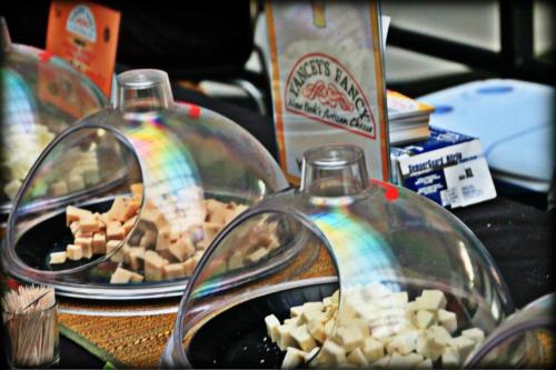 A display of assorted cheese cubes under glass domes, with a sign for "Tracy's Fancy" artisan cheese.