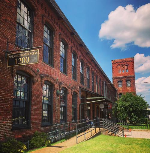Historic red brick building with large windows, featuring a sign for Marathon Motor Works and a tower in the background.