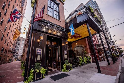 Exterior of Nicholson's Tavern, featuring flags, outdoor seating, and a charming urban setting at dusk.