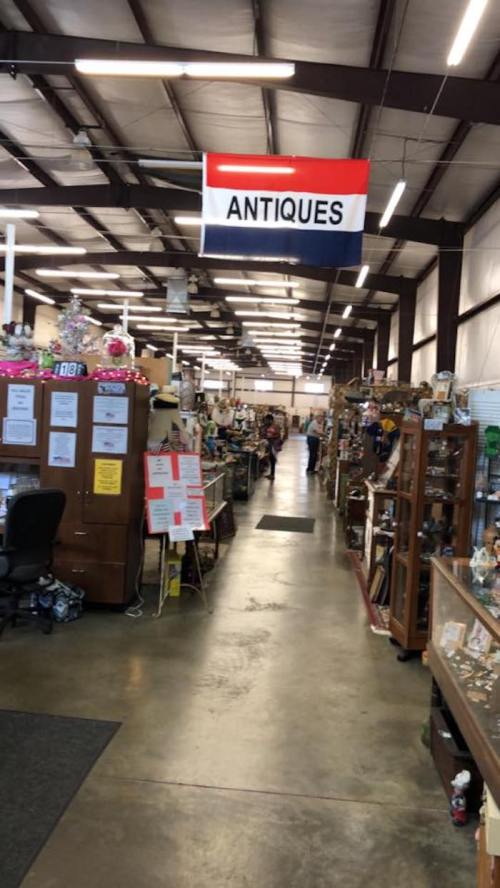 A spacious antique store aisle with various items for sale and a prominent "ANTIQUE" sign hanging above.