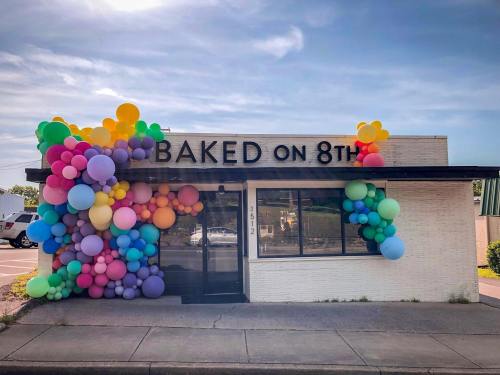 A storefront with the sign "BAKED on 8th," decorated with colorful balloons in various sizes.
