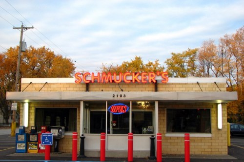 A storefront with the sign "Schmucker's" and an "OPEN" neon sign, surrounded by autumn trees.