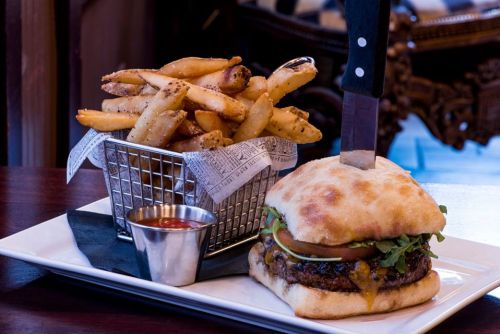 A juicy burger with cheese and toppings, served with a side of crispy fries in a basket and a small cup of ketchup.