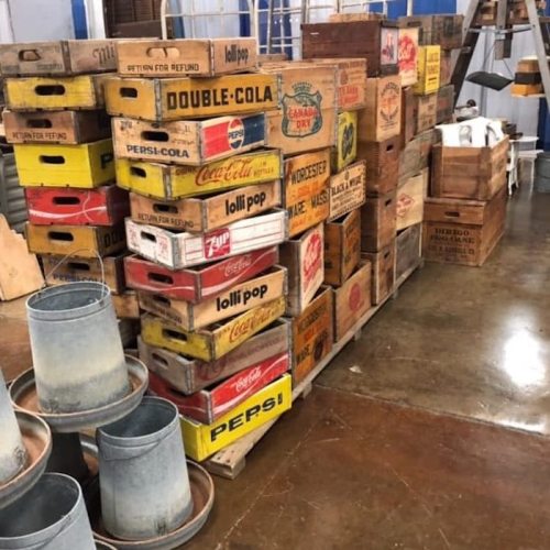 A stack of vintage wooden crates with various soda brands, including Coca-Cola and Pepsi, in a warehouse setting.