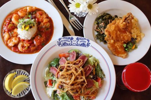 A table setting with three dishes: shrimp in sauce, fried chicken with greens, and a salad topped with crispy onions.