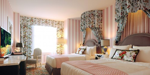 A bright hotel room with two beds, floral curtains, striped walls, and a TV, creating a cozy and inviting atmosphere.