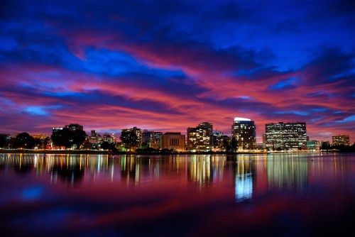 City skyline at dusk with vibrant pink and blue clouds reflected in the water, creating a serene atmosphere.