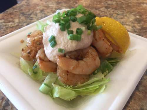 A plate of shrimp on lettuce, topped with a creamy sauce and green onions, garnished with a lemon wedge.