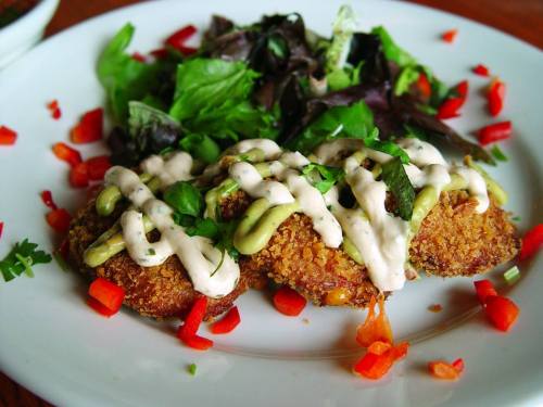 A plate of crispy fried food topped with creamy sauce, surrounded by fresh salad and diced red peppers.