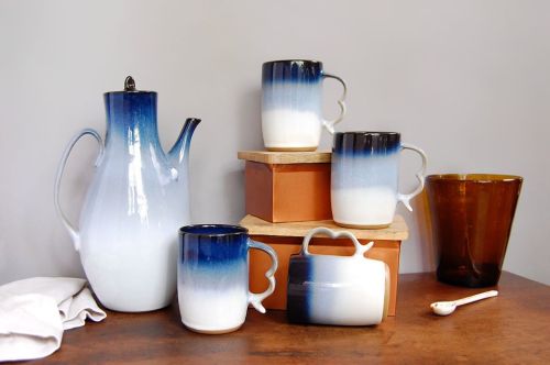 A ceramic tea set with a gradient blue and white design, featuring a teapot and four mugs on wooden blocks.
