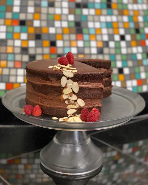 A chocolate cake with layers, topped with raspberries and almond slices, displayed on a silver cake stand.