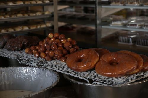 A display of freshly made donuts and small fried pastries on a cooling rack in a bakery.