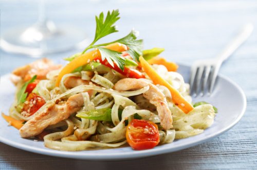 A colorful plate of pasta salad with chicken, cherry tomatoes, and bell peppers, garnished with parsley.