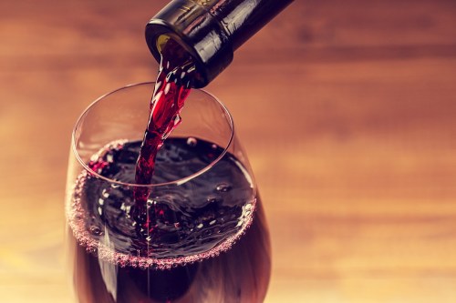 A bottle of red wine pouring into a glass, creating bubbles and ripples in the wine.