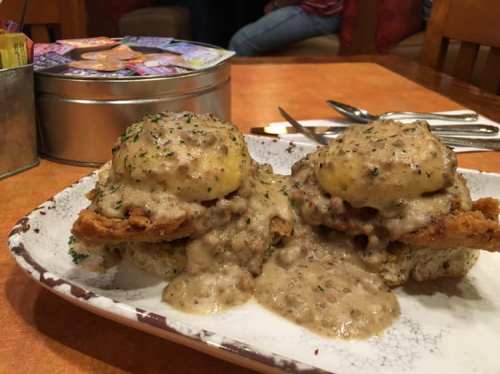 A plate of biscuits topped with fried chicken and smothered in creamy sausage gravy, garnished with parsley.