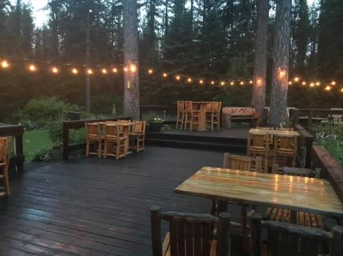 Cozy outdoor dining area with wooden tables and string lights, surrounded by tall trees in a serene setting.