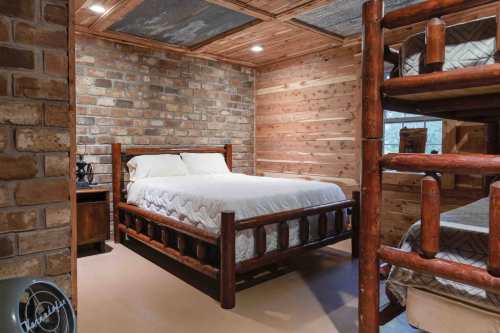 Cozy bedroom featuring a wooden bed, bunk beds, and rustic brick and wood walls. Warm, inviting atmosphere.