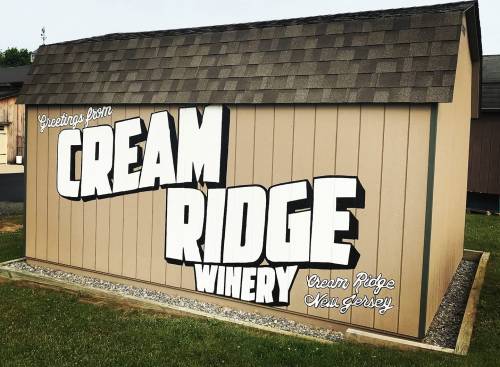 A wooden shed with a sign reading "Greetings from Cream Ridge Winery, Cream Ridge, New Jersey" in bold letters.