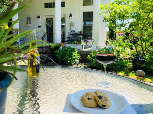 A glass of red wine and chocolate chip cookies on a table, with a garden and a house in the background.