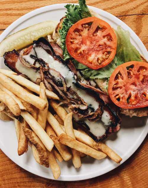 A plate of bacon cheeseburger with lettuce, tomato, pickles, and a side of golden French fries.