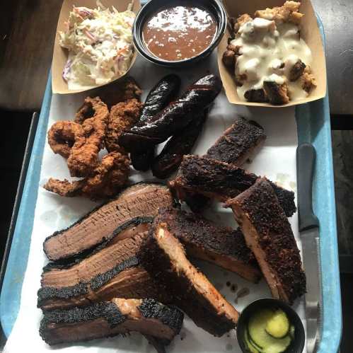 A platter of barbecue featuring brisket, sausage, fried chicken, coleslaw, baked beans, and dessert.