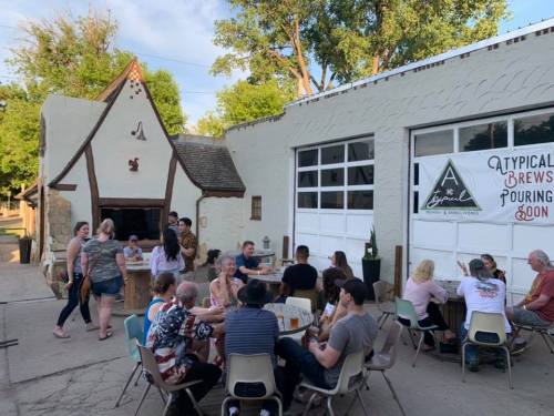 A lively outdoor gathering at a brewery, with people socializing and enjoying drinks in a sunny setting.