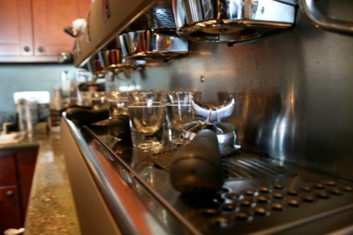 Close-up of an espresso machine with portafilters and glass cups on a countertop.
