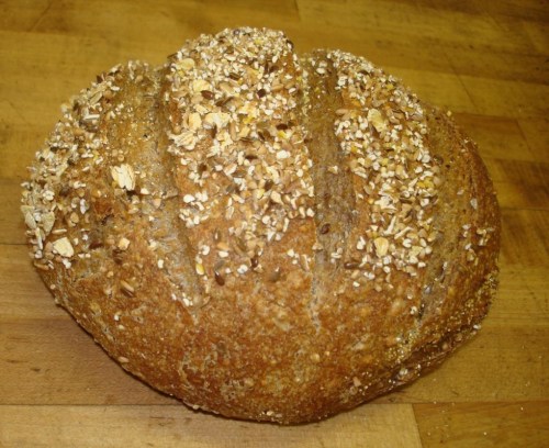 A round loaf of bread topped with oats and seeds, resting on a wooden surface.