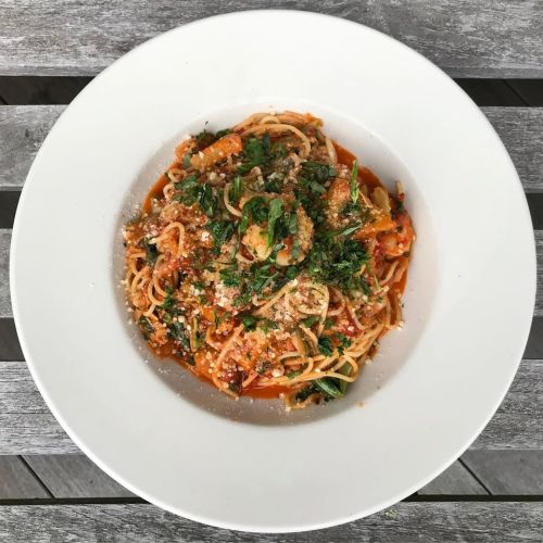A bowl of spaghetti topped with tomato sauce, herbs, and grated cheese, served on a wooden table.
