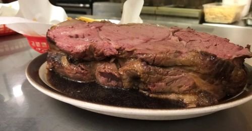 A large, juicy slice of prime rib served on a plate, with a rich brown sauce underneath.