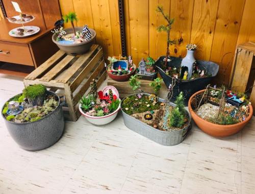 A collection of decorative potted plants and miniature scenes arranged on a floor, with wooden and metal containers.