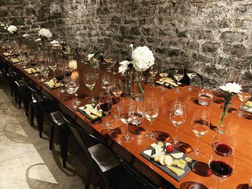 A long wooden table set with wine glasses, cheese platters, and flowers in a rustic stone-walled setting.