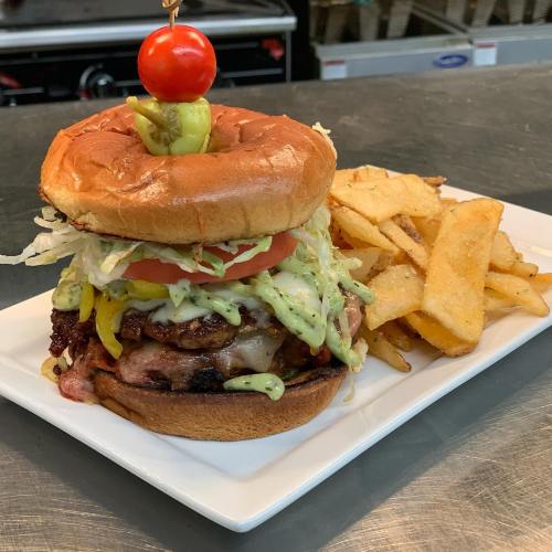 A juicy burger with lettuce, tomato, pickles, and sauce, served with golden fries on a white plate.