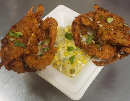 Fried crab claws served with a creamy corn dish, garnished with green onions on a white plate.
