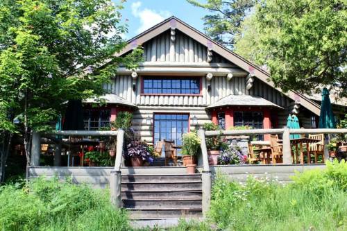 A charming log cabin-style restaurant surrounded by greenery and colorful flowers, featuring outdoor seating.