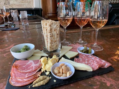 A charcuterie board with meats, cheeses, olives, nuts, and crackers, accompanied by three glasses of rosé wine.