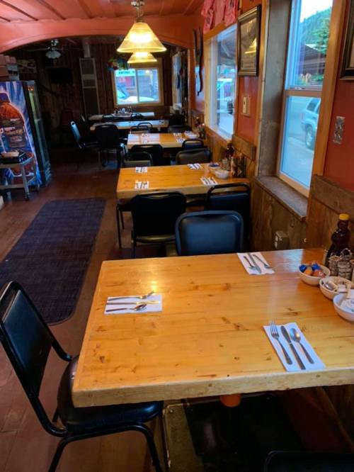 Interior of a cozy restaurant with wooden tables set for dining, featuring black chairs and warm lighting.