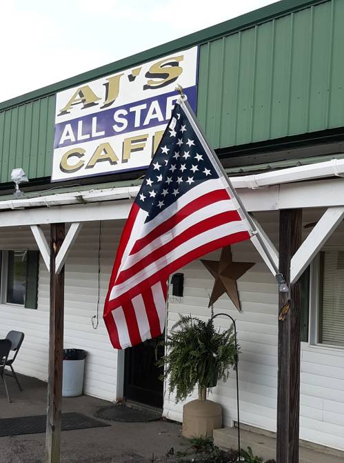 A U.S. flag waves in front of AJ's All Star Café, featuring a green roof and a star decoration.