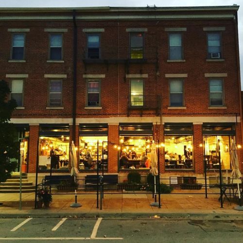 A cozy brick restaurant with warm lights, bustling diners, and outdoor seating on a quiet street at dusk.
