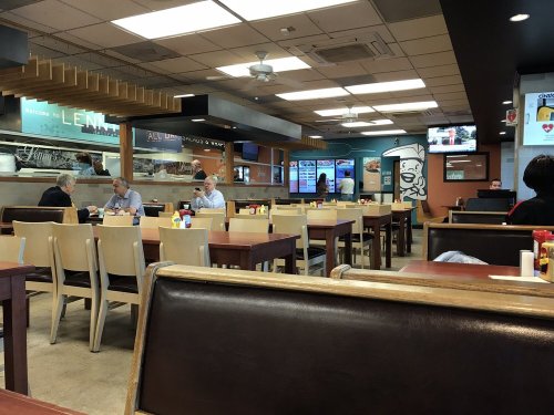 Interior of a casual dining restaurant with tables, chairs, and customers eating. TVs are mounted on the walls.